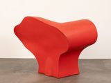 a red chair sitting on top of a cement floor next to a white wall