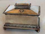 une boîte ancienne en métal argenté avec un couvercle, posée sur une surface blanche