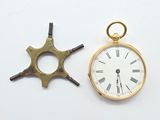 une montre de poche en or et une petite horloge posées sur une surface blanche