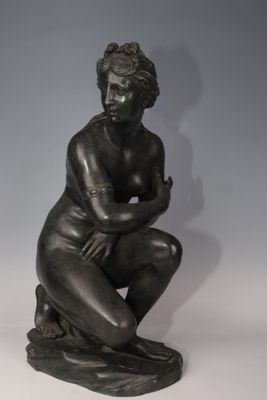 bronze statue of a female nude sitting on a rock with her arms crossed