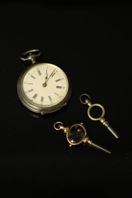 a pocket watch and a key on a black surface