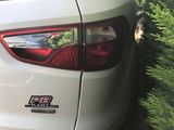 the rear end of a white car parked next to a bush