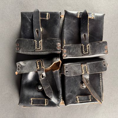 four black leather pouchs on a gray surface with one open