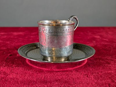 une tasse et une soucoupe en argent posées sur une nappe rouge