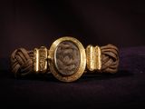 a close up of a gold bracelet with a roman coin on it