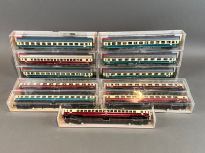 Plusieurs trains miniatures sont empilés dans des boîtes en plastique posées sur une surface grise