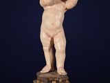 an antique statue of a baby on a pedestal with a clock in the background