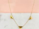 un collier plaqué or posé sur une surface en marbre, sur fond rose