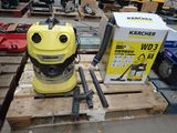 un aspirateur jaune posé sur une palette, à côté d'une caisse d'outils