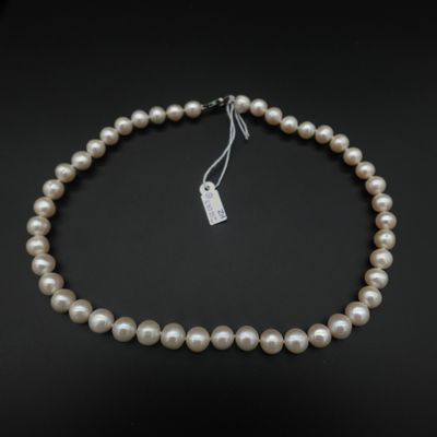 un collier de perles blanches muni d'un fermoir en argent, sur fond noir