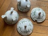 three white dishes with green flowers on them sitting on a wooden floor