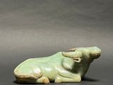 a green statue of a cow laying down on a black surface