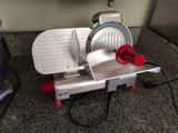 a silver and red food slicer on a counter top