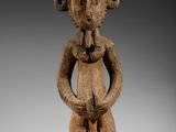 une image représentant une statue en bois d'un homme les mains dans les poches