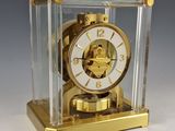 une horloge dorée dans un écrin transparent posé sur une surface blanche