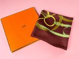 a brown and green scarf and orange box on a pink surface
