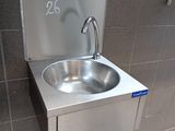 a stainless steel sink in a public restroom with a paper towel dispenser attached to the wall