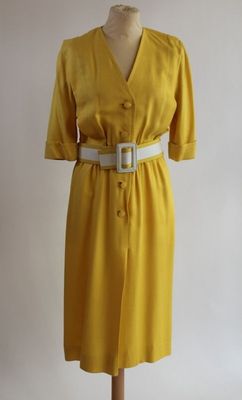 robe jaune posée sur un présentoir à mannequin, avec une ceinture blanche