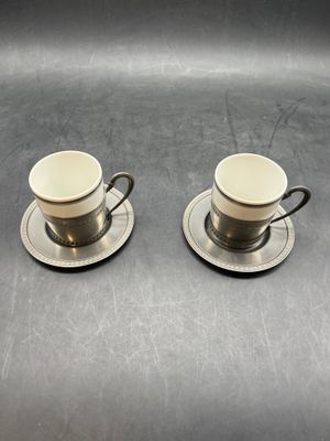 two cups and saucers sitting on top of a metal table