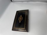 un petit livre noir aux bords dorés posé sur une table blanche