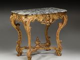 une table richement sculptée, avec un plateau en marbre reposant sur un socle gris