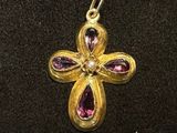 an image of a gold cross with pink stones on a black surface