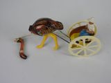 une figurine représentant une autruche tirant une charrette sur laquelle se trouve un homme