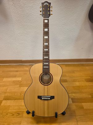 une guitare acoustique posée sur un support en bois, sur un parquet en bois massif