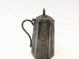 une cafetière en argent avec une anse, posée sur une surface blanche
