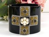 black cuff bracelet with pearls and crosses on it next to flowers