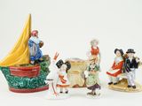 several figurines of people standing around a boat on a white surface