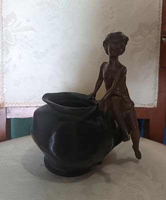 une statue représentant une femme assise sur un vase posé sur une table