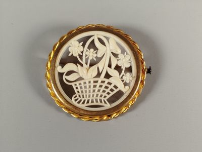 une image représentant une broche blanche et dorée sur laquelle est représenté un panier de fleurs