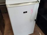 a small white refrigerator sitting in a room next to a shelf