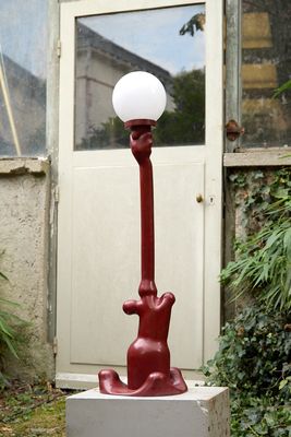 un lampadaire rouge surmonté d'un chat, devant une porte