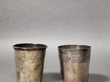 two silver cups with designs on them sitting on a table