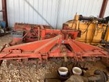 a red tractor with a plow in front of a building