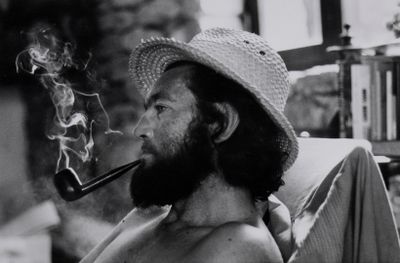 photographie en noir et blanc d'un homme coiffé d'un chapeau et fumant la pipe