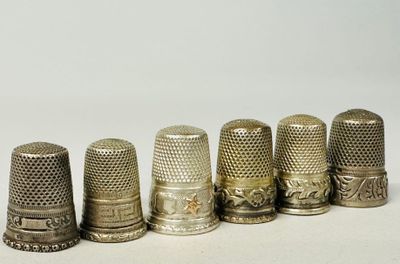 six antique thimbles lined up in a row on a white surface