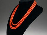 an orange beaded necklace is displayed on a black mannequin