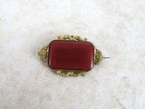 a close up of a red and gold broochle on a white surface