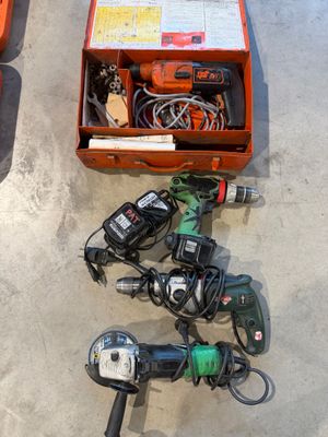 une boîte à outils posée par terre à côté de deux perceuses