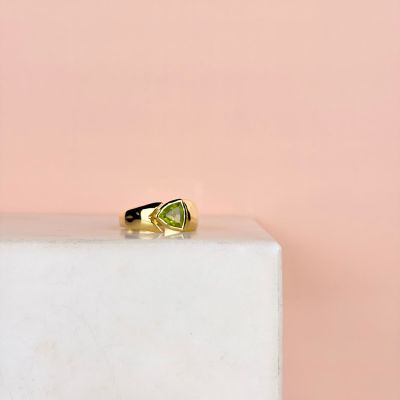 une bague en or sertie d'un péridot posée sur un bloc de marbre