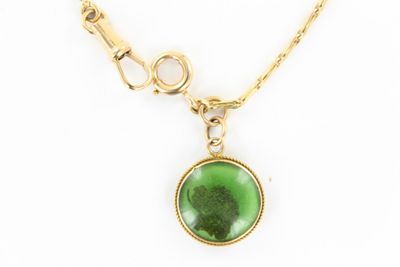 un gros plan d'un collier composé d'une pierre verte montée sur une chaîne en or