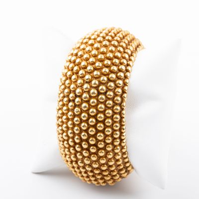 a close up of a gold beaded bracelet on a white surface