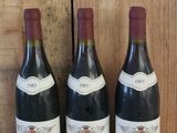 trois bouteilles de vin sont posées sur une étagère en bois devant un mur en bois