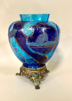 a blue glass vase with a gold base on a table