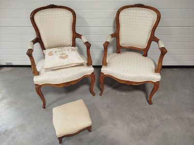 two chairs and a foot stool in a room with a white wall