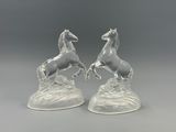 paire de figurines de chevaux en verre transparent posées sur un rocher