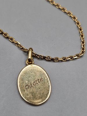un gros plan d'un collier plaqué or sur lequel est gravé le mot « odalate »
